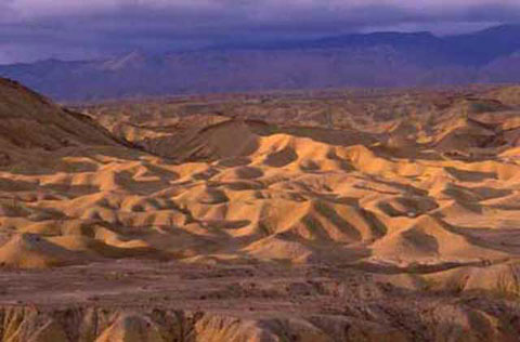 Color photo of the Fish Creek-Vallecito Badlands and western mountains, taken from the Wind Caves